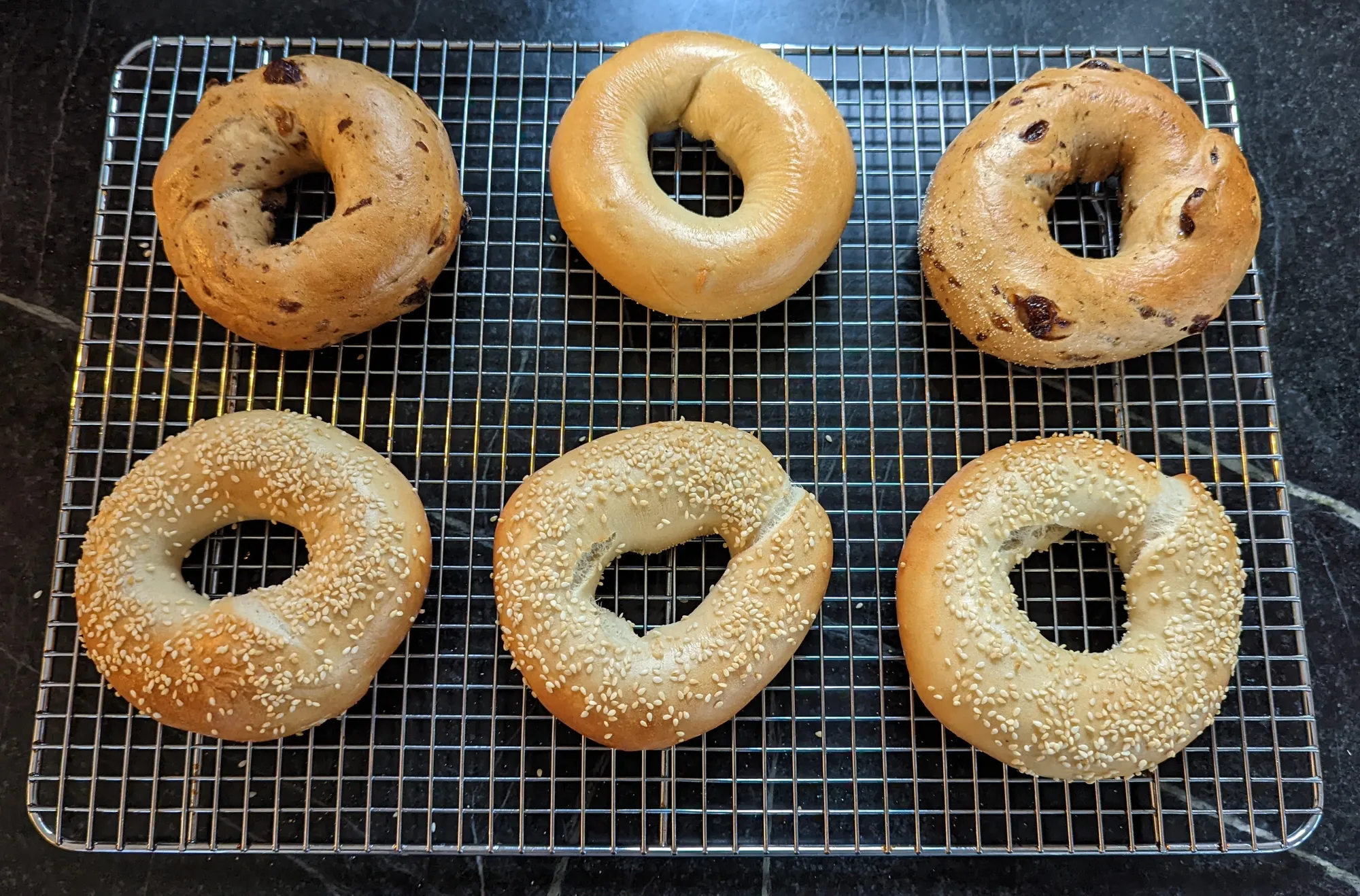 Finished cinnamon-raisin, plain and sesame bagels on a cooling rack.